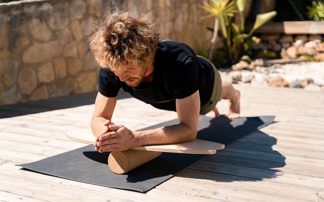 Mann beim Bauchmuskeltraining mit Balance Board aus Holz auf Korkrolle