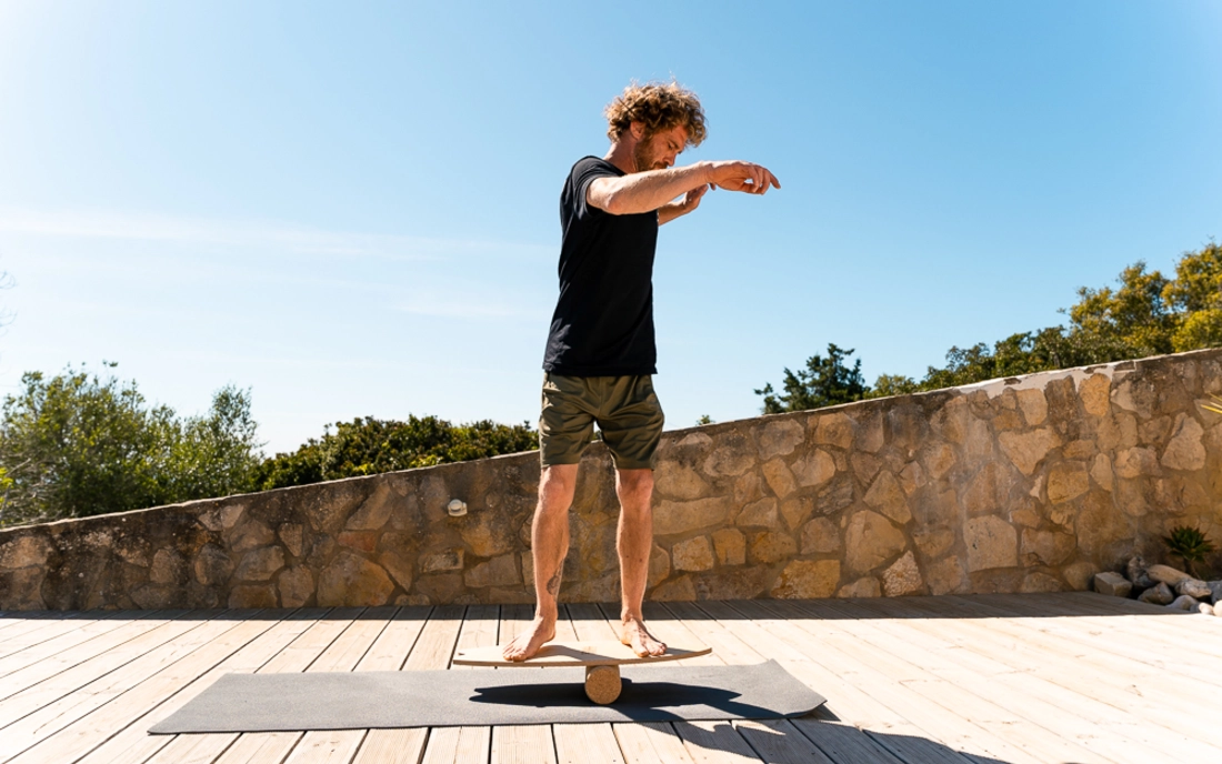 Mann beim Surfworkout auf Balance Board aus Holz mit Korkrolle