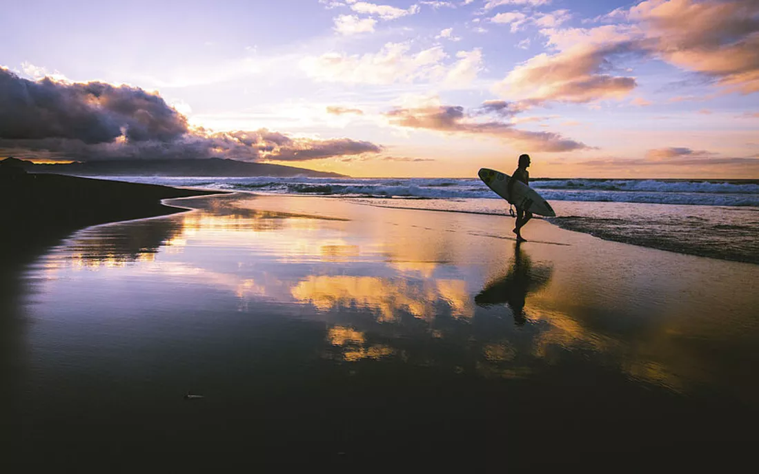 Surferin mit Surfbrett bei Sonnenuntergang am Strand