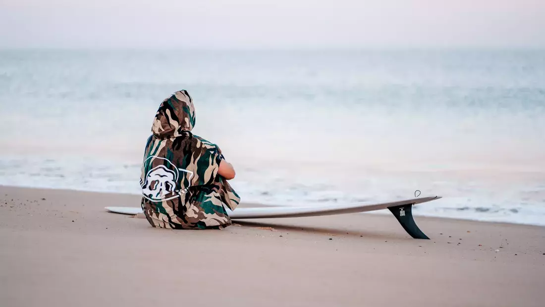 mann im surfponcho sitzend vorm meer