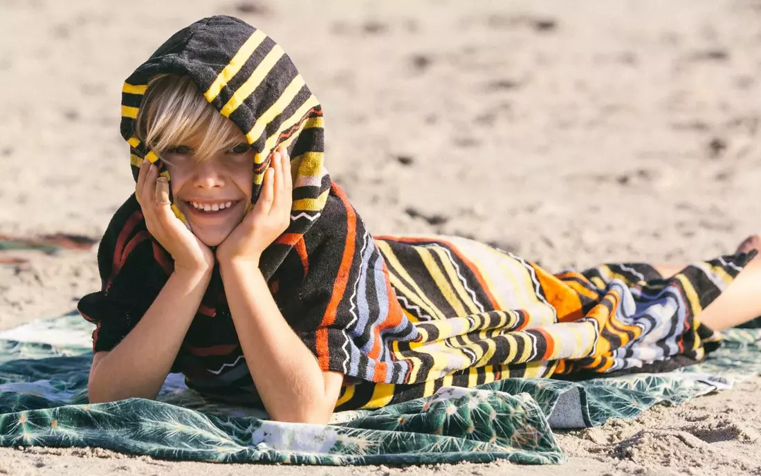 Kleiner Junge liegt im Surf Poncho am Strand