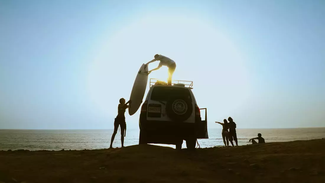 Landrover off shore with two people loading a surfboard onto the roof