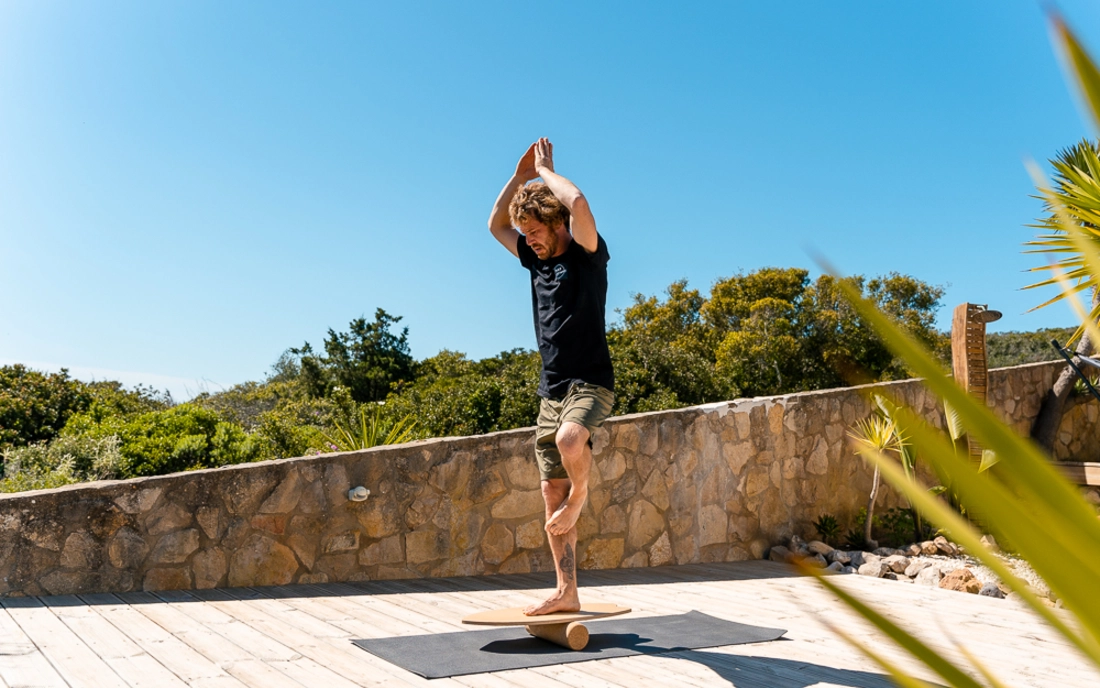 Mann bei Yoga auf Balance Board aus Holz mit Korkrolle