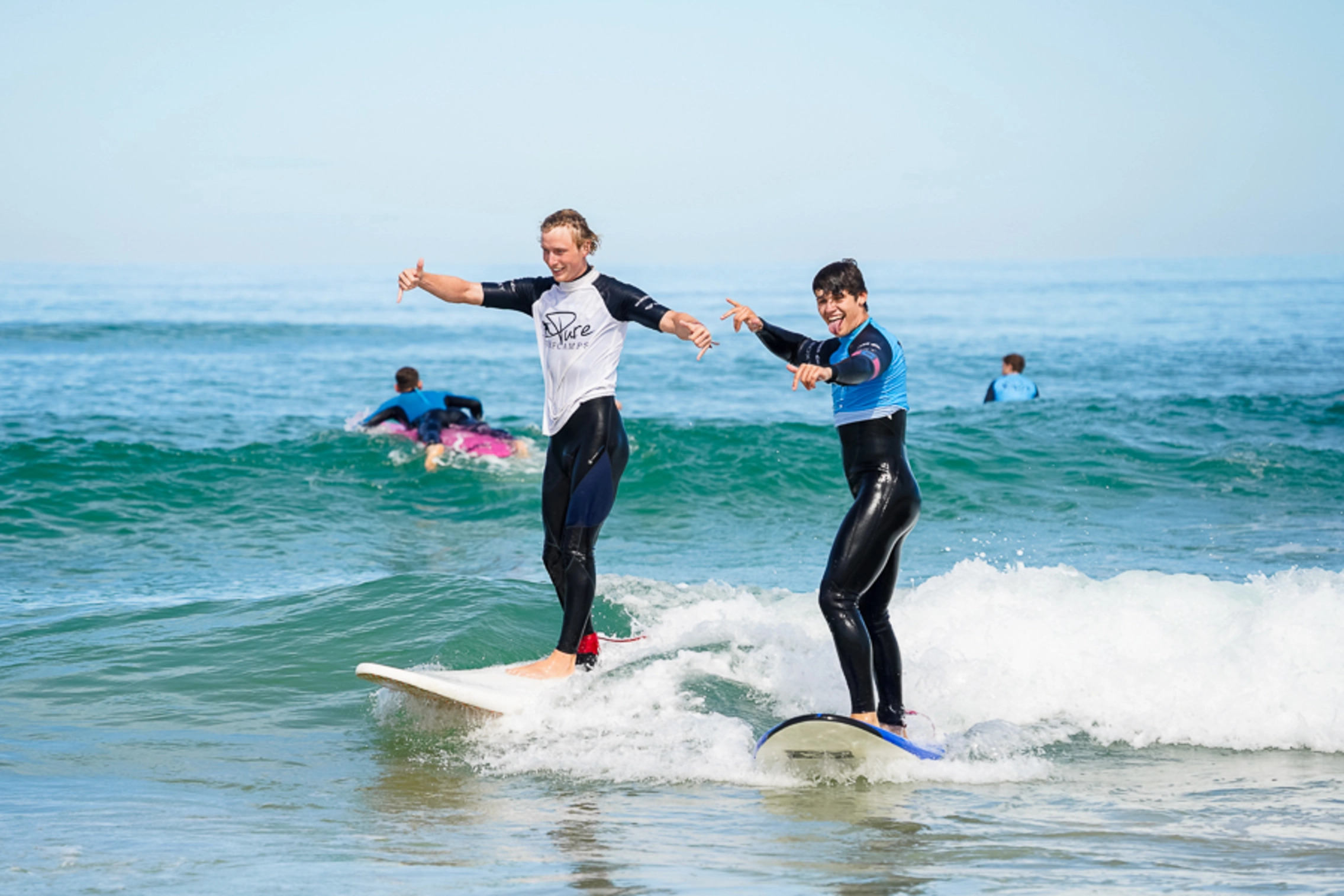 Surflehrer surft gemeinsam mit Surfschüler eine Welle