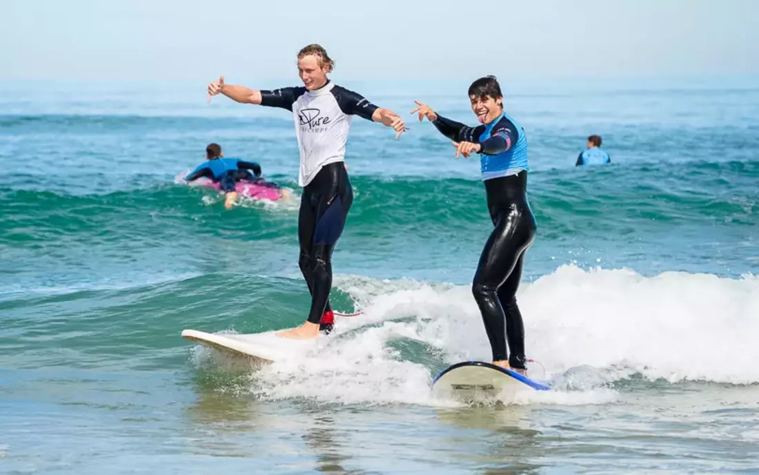 Surflehrer surft gemeinsam mit Surfschüler eine Welle