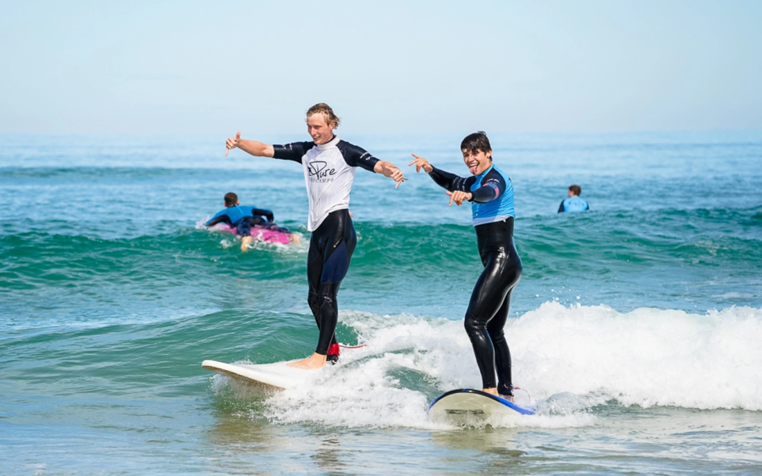 Surflehrer surft gemeinsam mit Surfschüler eine Welle