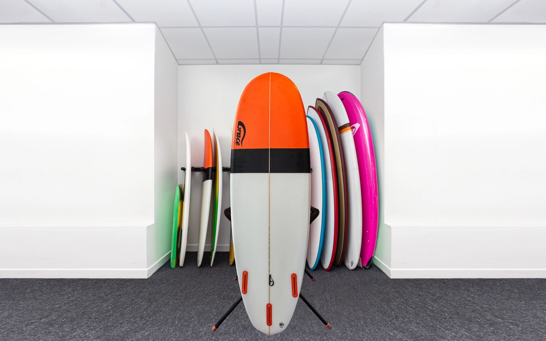 Grau orangenes Hybrid Surfbrett vor einer Reihe Surfboards