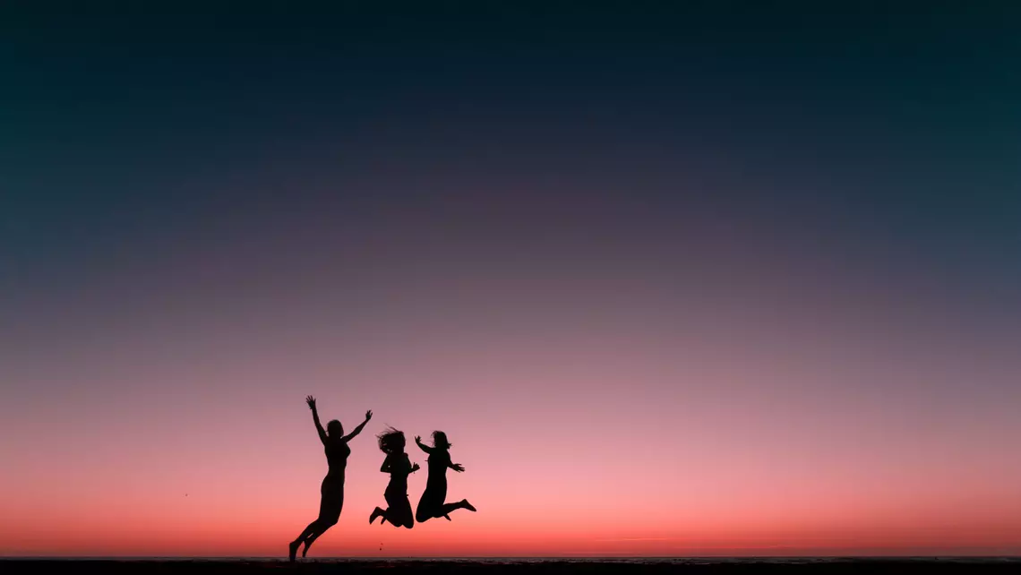 Gruppenfoto Freundinnen springen vor Sonnenuntergang am Meer in die Luft