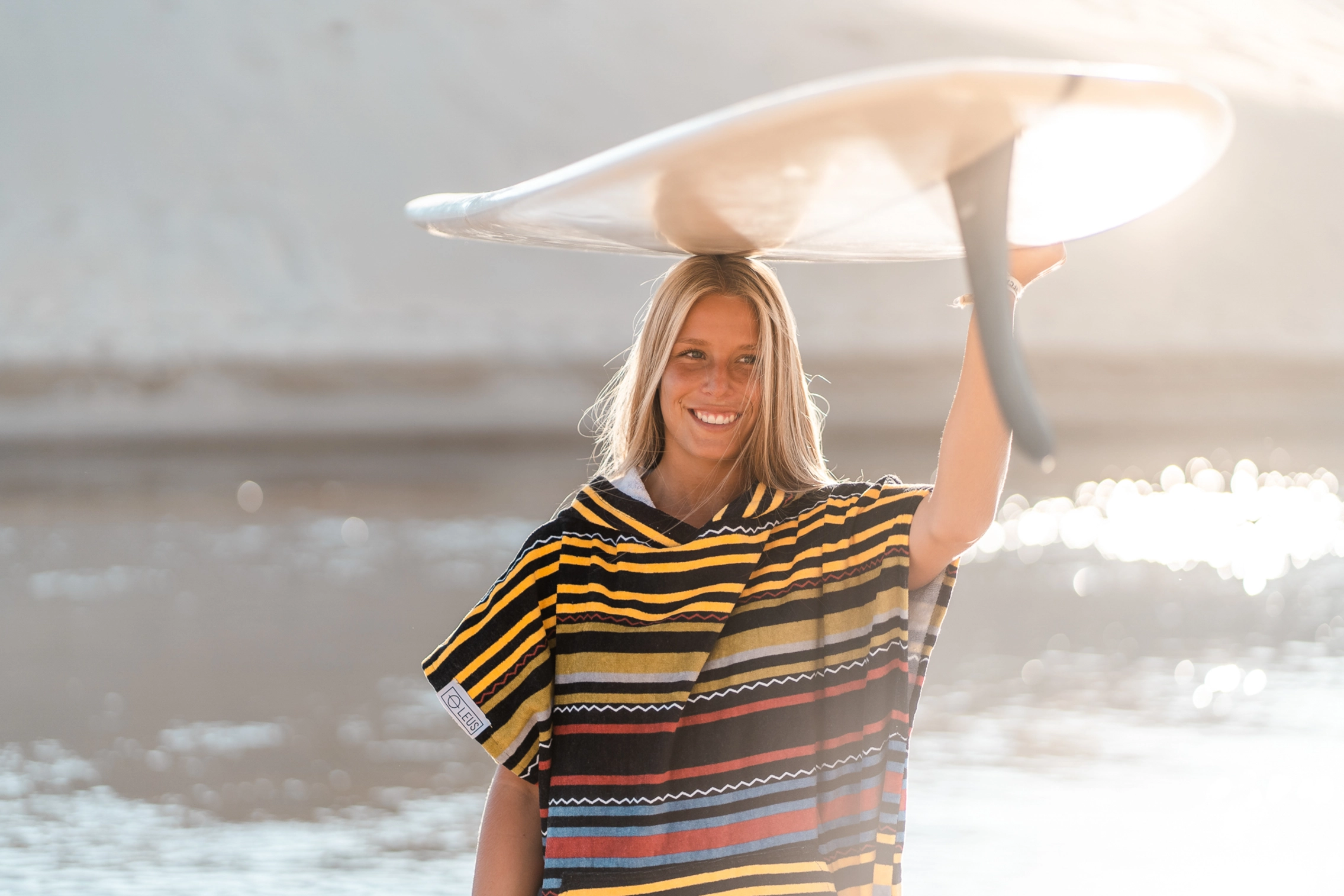 Surferin im Surf Poncho mit Surfbrett auf dem Kopf am Strand