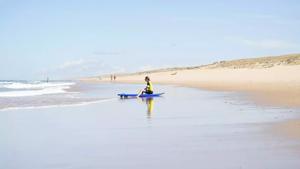 Surfschülerin sitzt am Wasserrand 