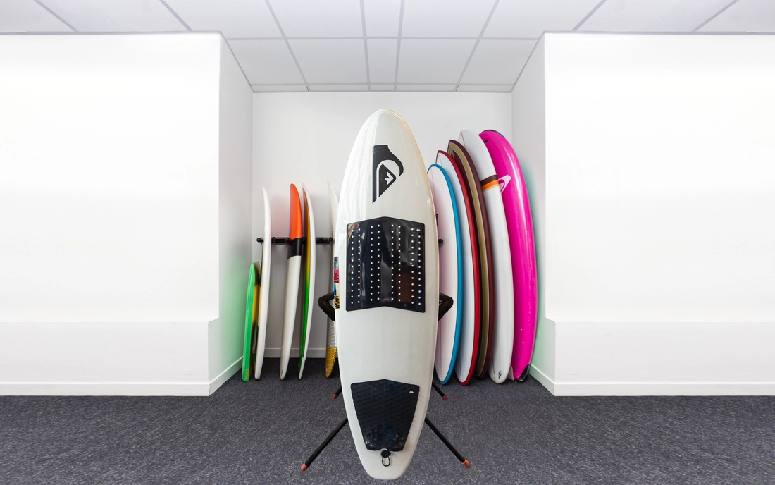 Weißes Softtop Hybrid Surfbrett vor einer Reihe Surfboards