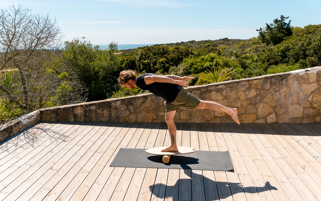 Mann bei Yoga auf Balance Board aus Holz mit Korkrolle