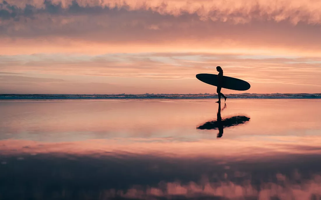 Surferin mit Surfbrett bei Sonnenuntergang am Strand