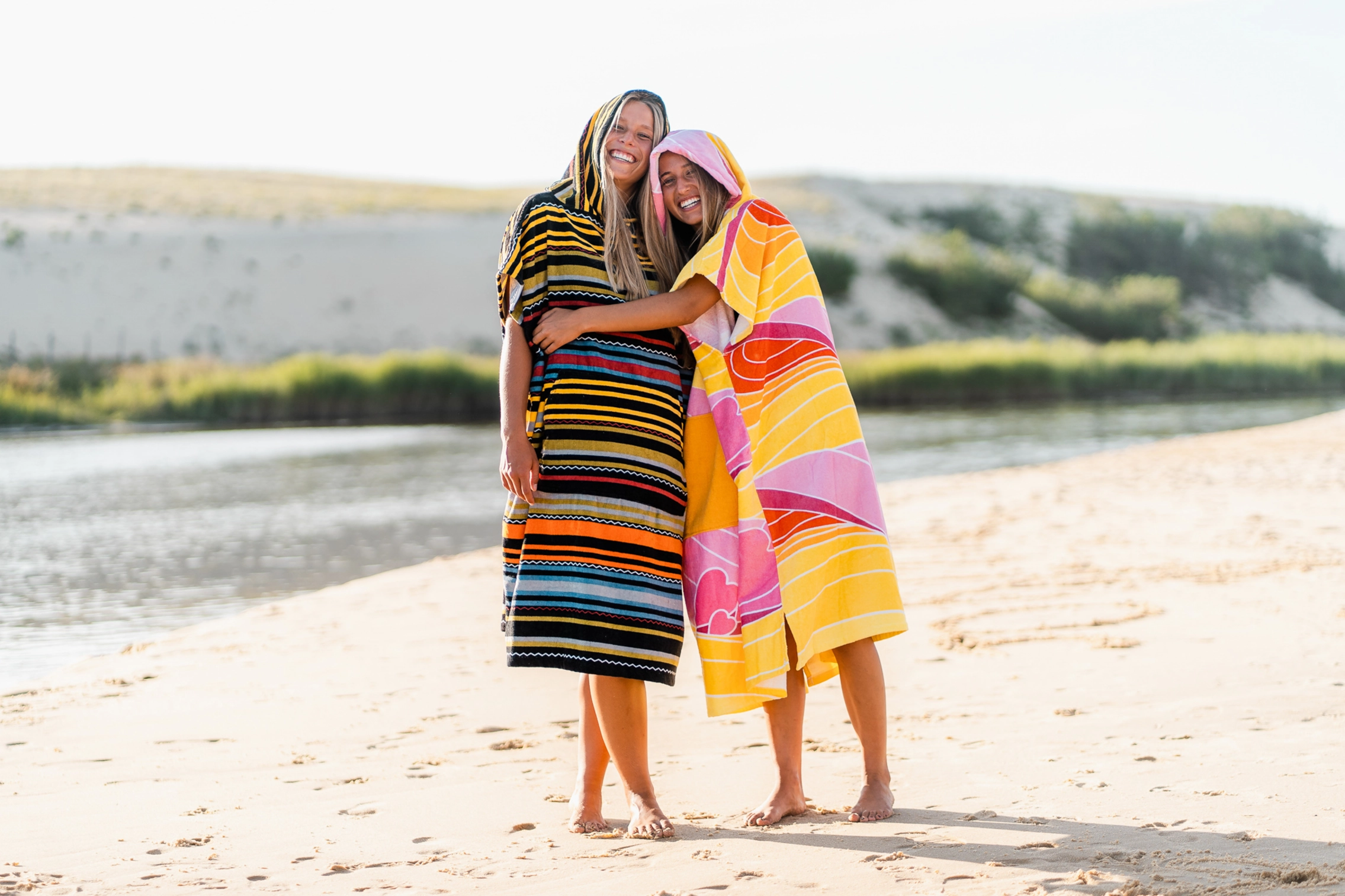 Surferinnen umarmen sich im Surf Poncho am Strand