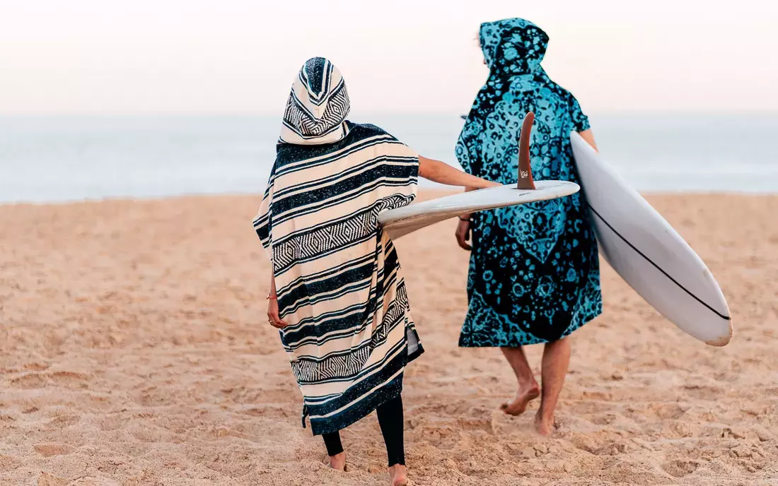 surfer in surf poncho mit surfboard unter dem arm laufen ueber strand