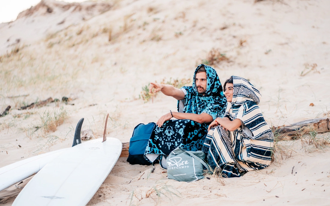 surfer sitzen im surfponcho und mit surfbrettern am strand