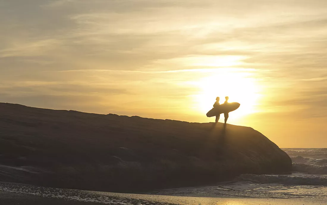 Surfer mit Surfbrett beim Sonnenuntergang an Klippe