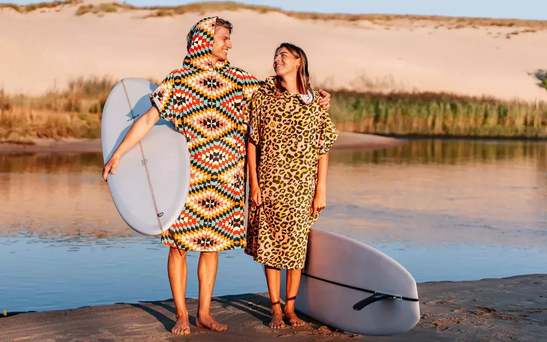 surfer stehen in gemustertem surfponcho und mit surfbrett vor fluss