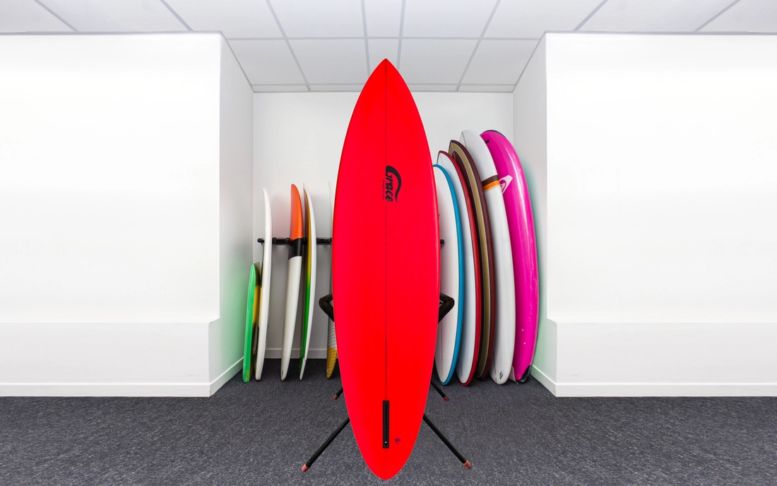 Rotes Single Fin Surfbrett vor einer Reihe Surfboards