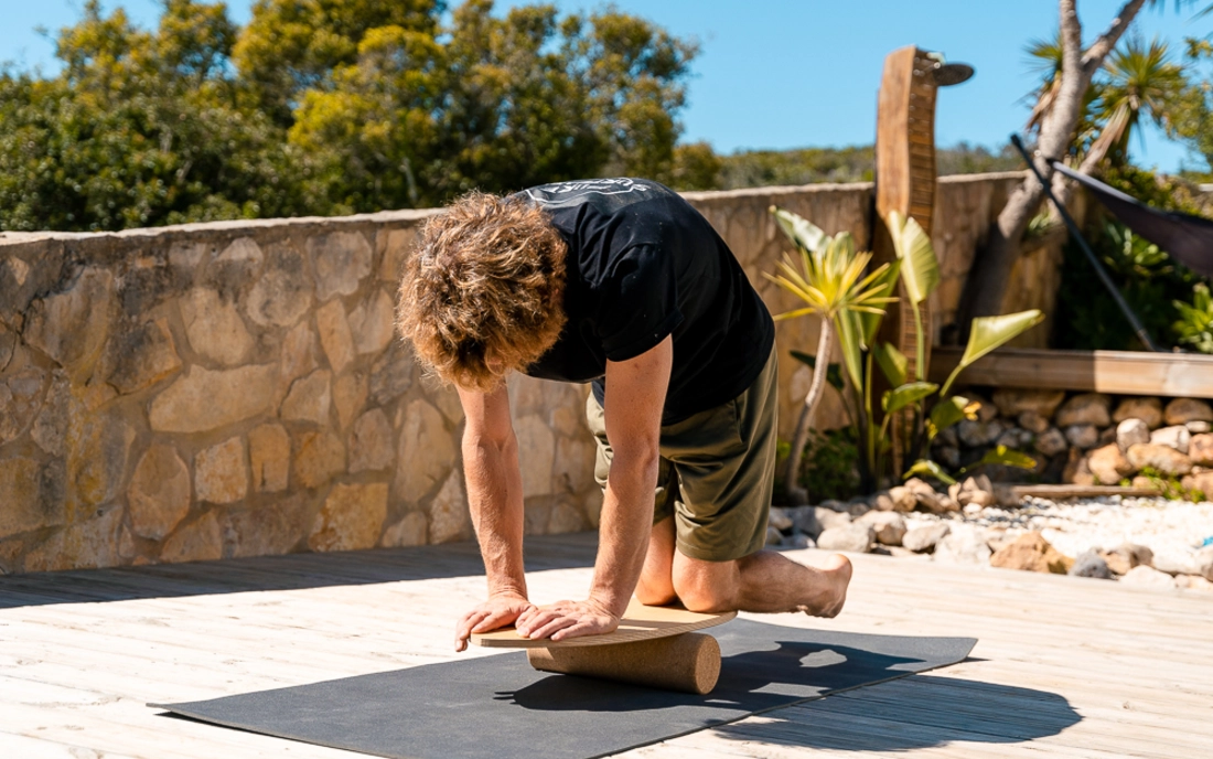 Mann bei Yoga auf Balance Board aus Holz mit Korkrolle