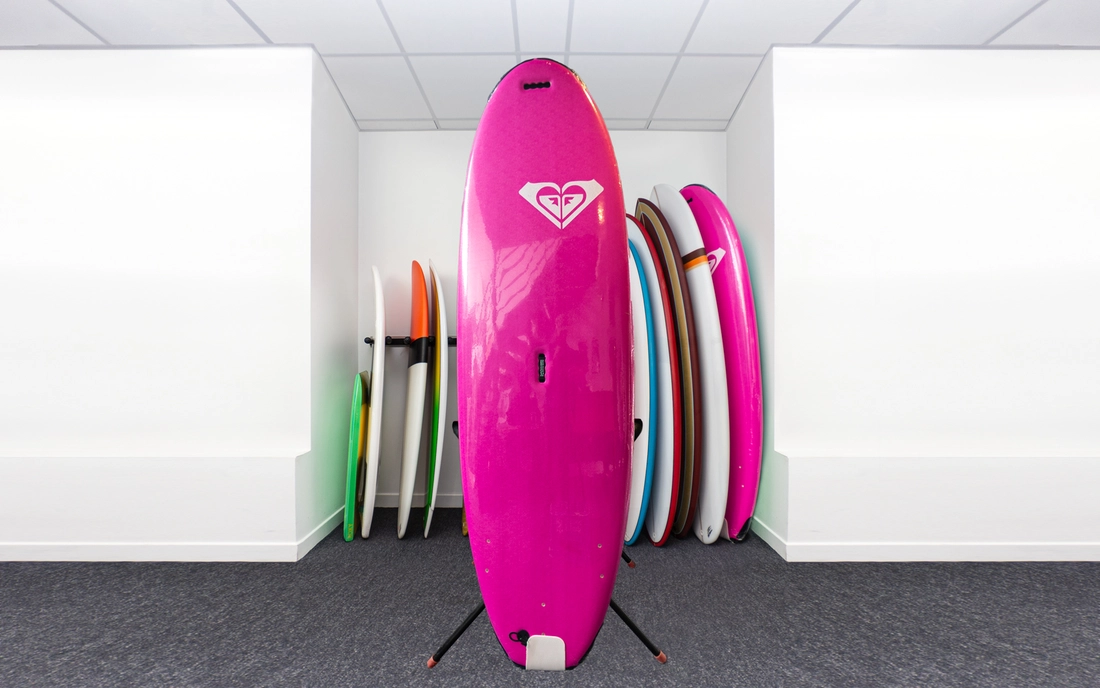 Pinkes Softtop Mini Malibu vor einer Reihe Surfboards