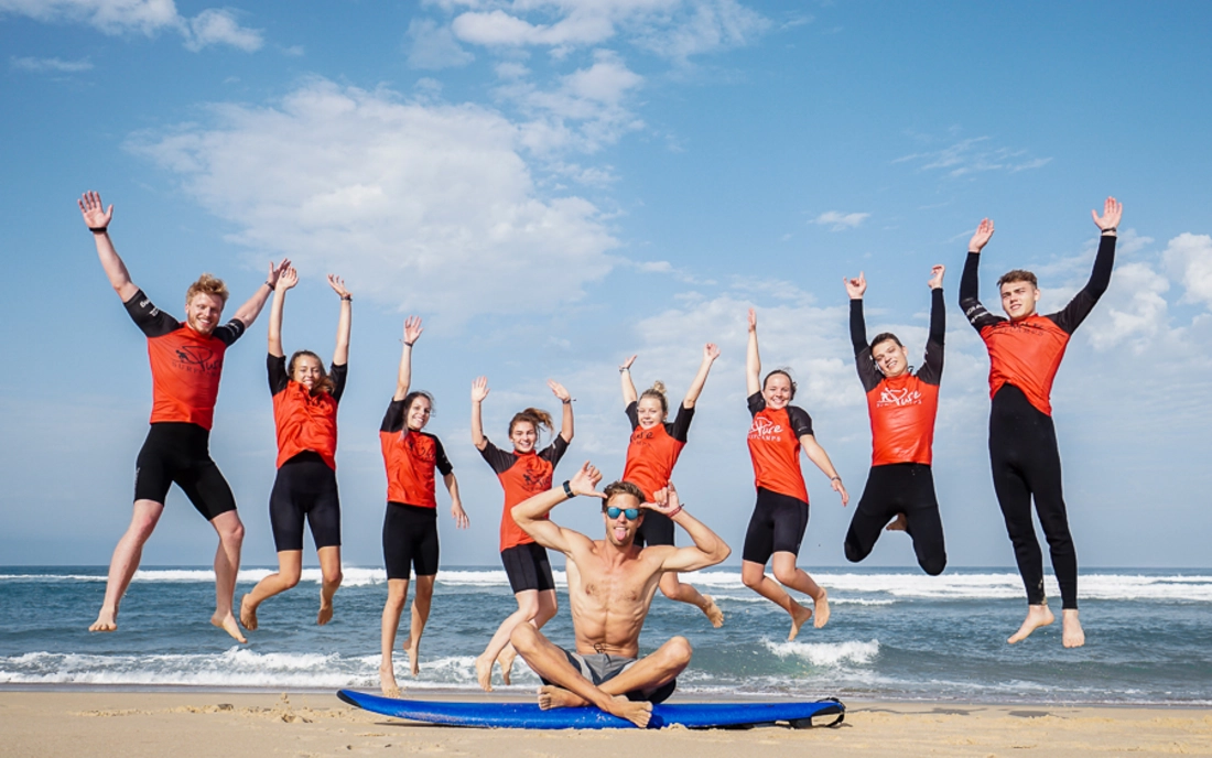 Surfkurs mit Surflehrer beim Gruppenfoto am Strand