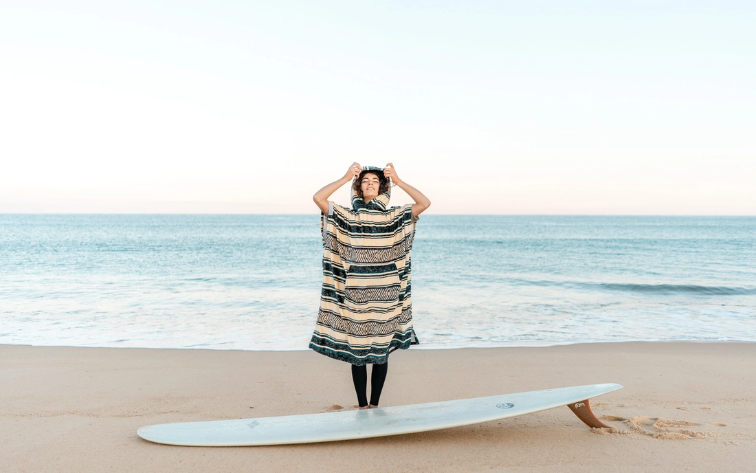 frau in beige schwarz gemustertem surf poncho vor dem meer