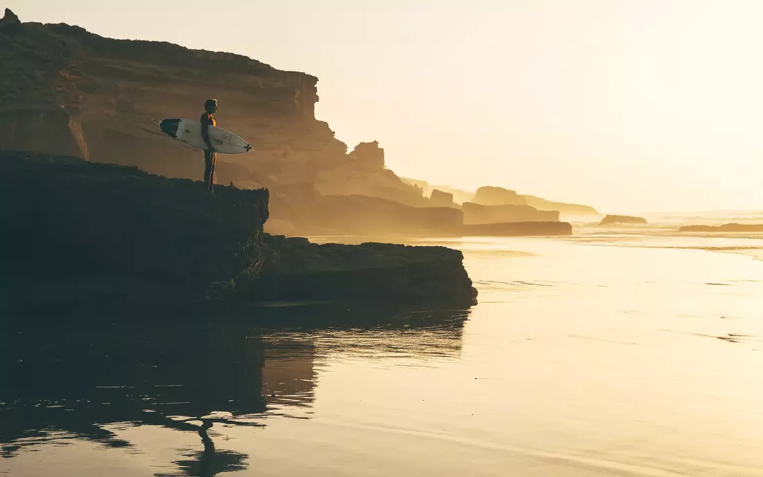 Finn Springborn mit Surfboard auf Fels