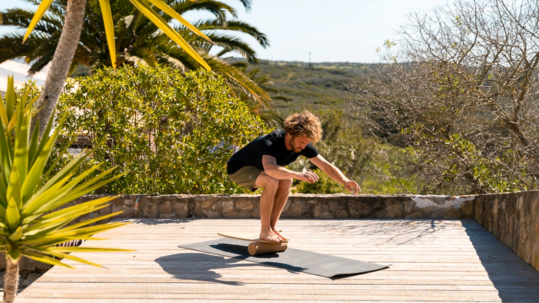 Mann beim Surfworkout auf Balance Board aus Holz mit Korkrolle