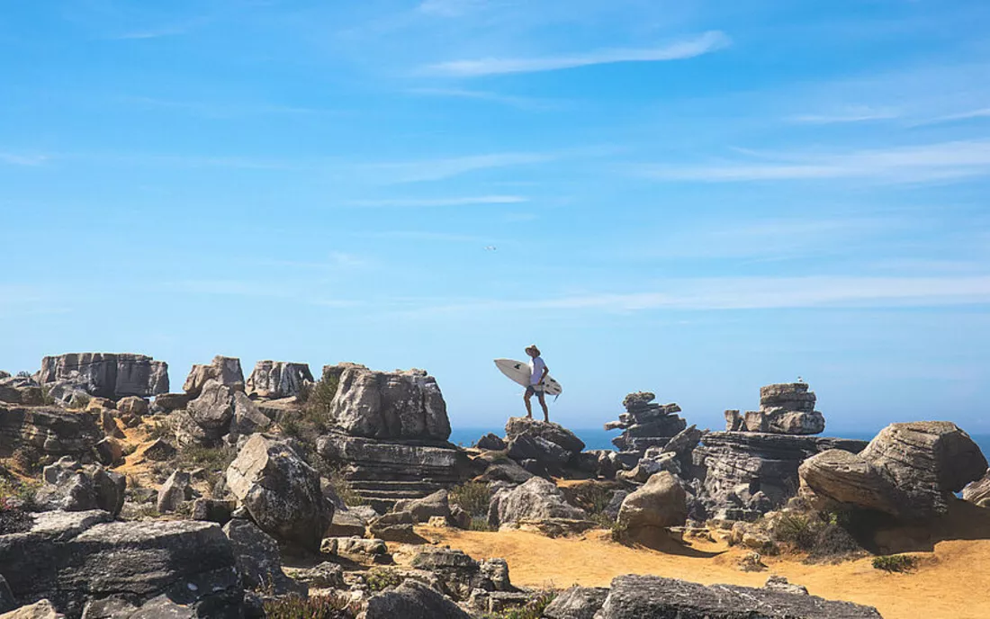 Surfer mit Surfbrett am Strand mit Felsen