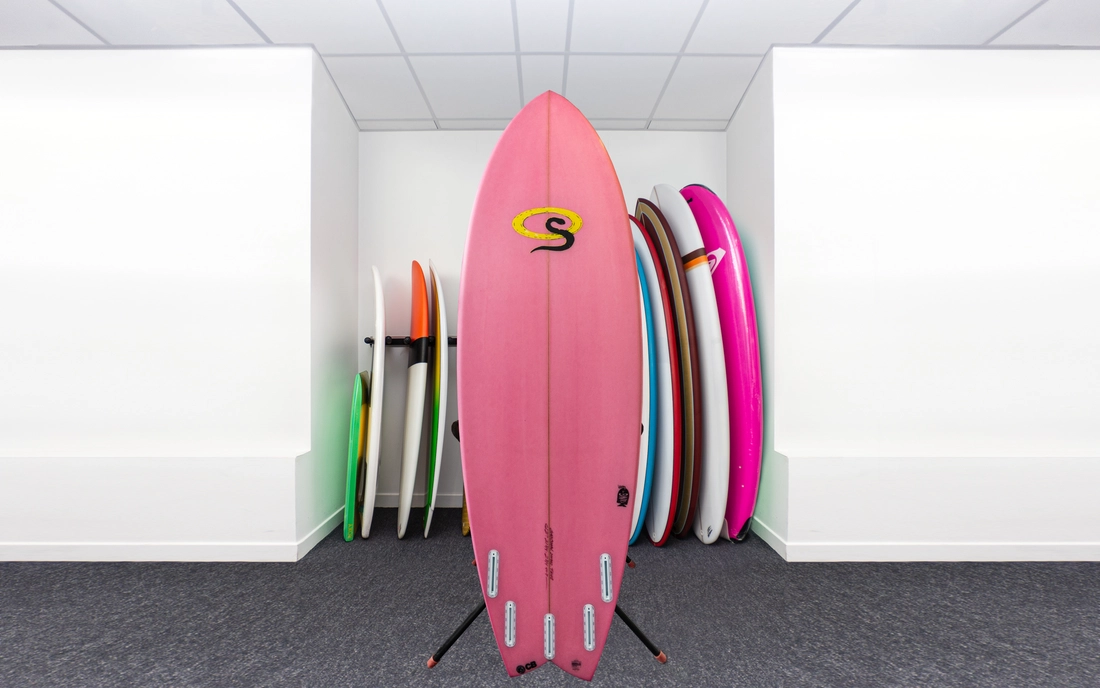 Rosa Hybrid Surfbrett vor einer Reihe Surfboards