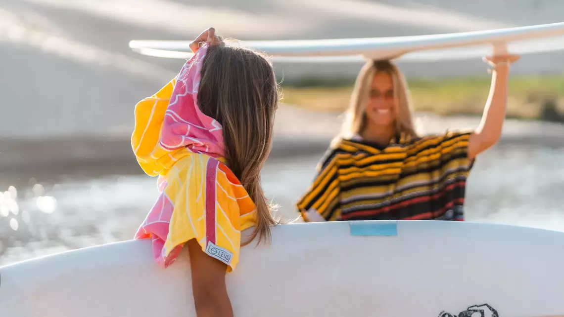 Surferinnen im Surf Poncho und mit Surfbrett am Strand