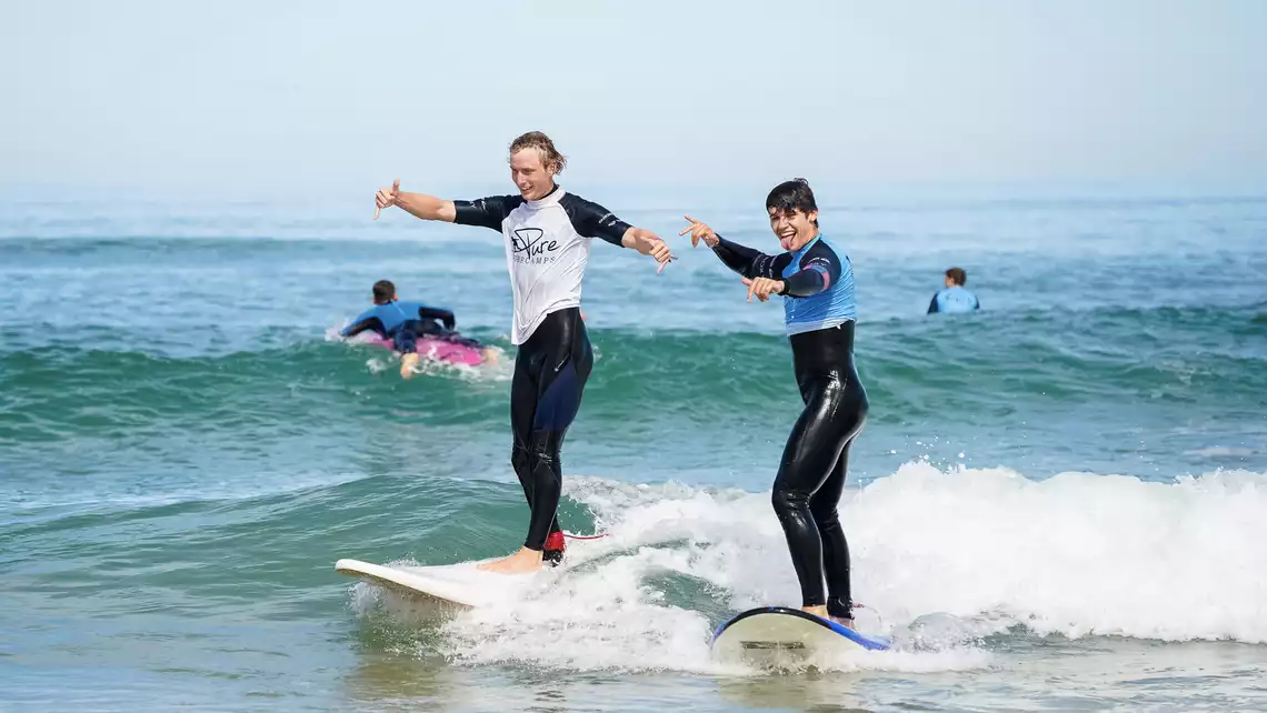 Surfschüler und Surflehrer surfen gemeinsam eine Welle