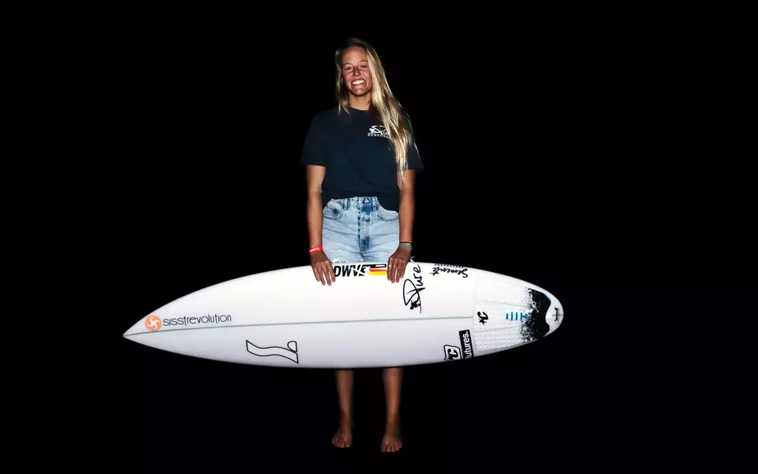 Puresurfcamps Pro Surf Teamriderin Camilla Kemp mit Surfboard vor schwarzem Hintergrund