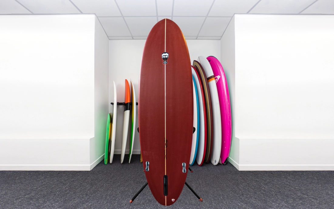 Rotbraunes Mid Length Surfbrett vor einer Reihe Surfboards