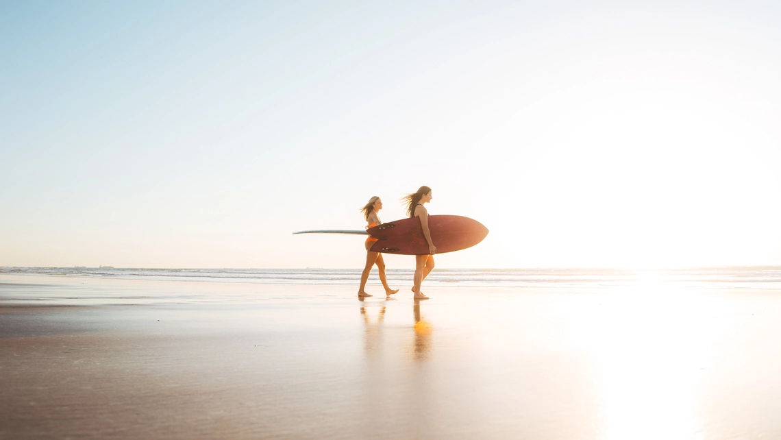 Frauen mit Surfbrett unterm Arm am Strand zum Sonnenuntergang