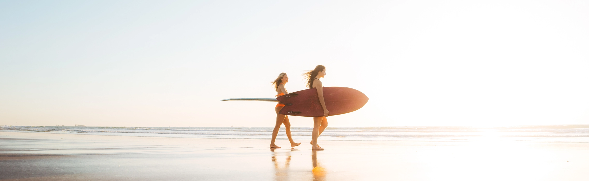 Frauen mit Surfbrett unterm Arm am Strand zum Sonnenuntergang