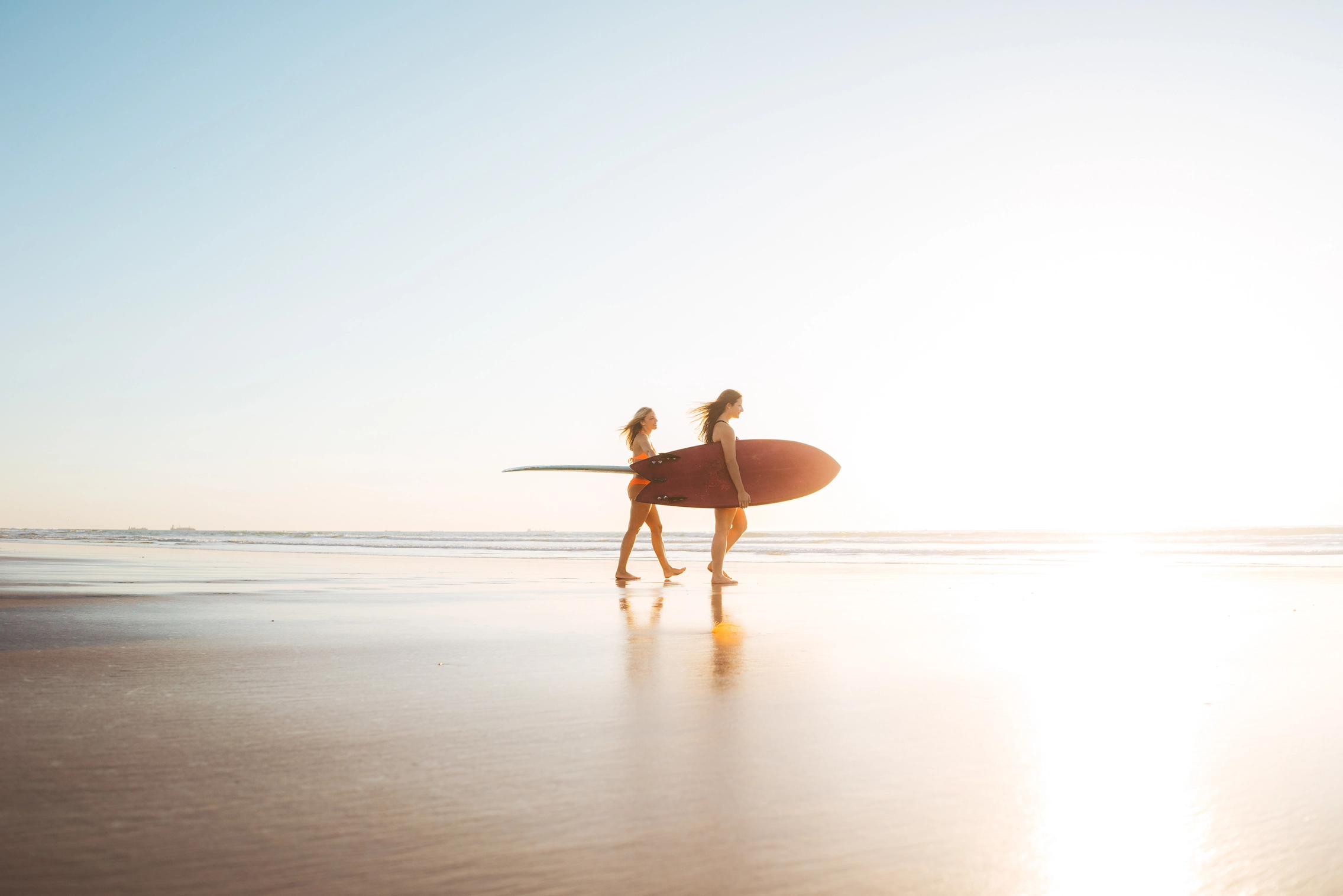 Frauen mit Surfbrett unterm Arm am Strand zum Sonnenuntergang