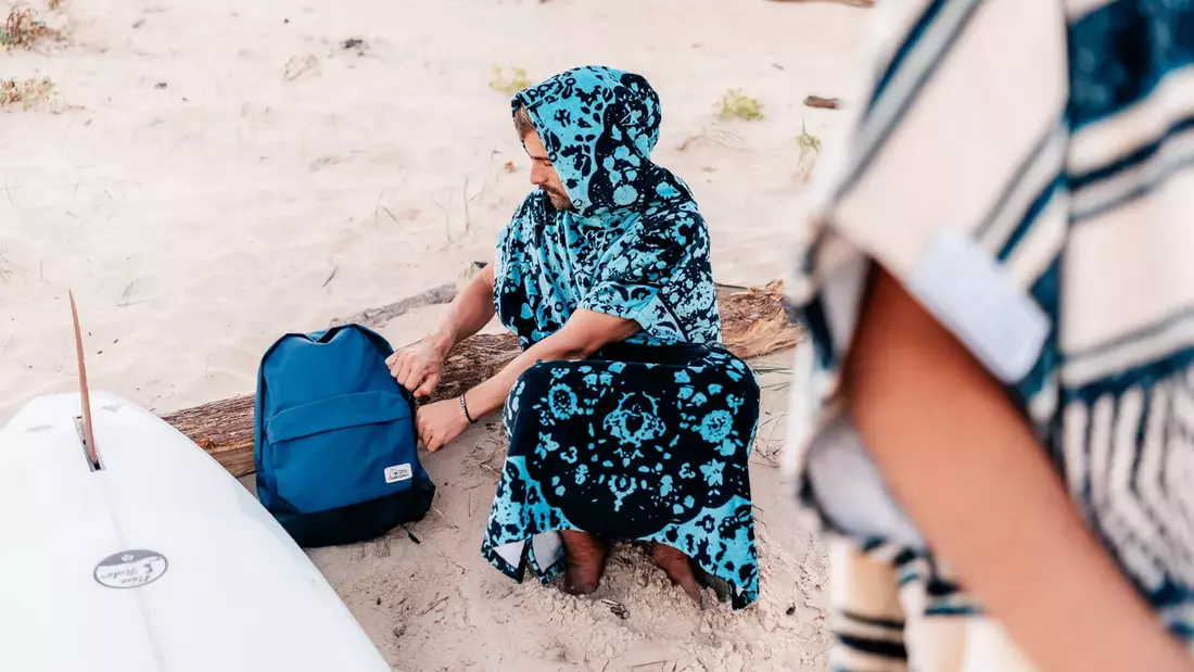 mann in blau gemustertem surfponcho sitzt am strand